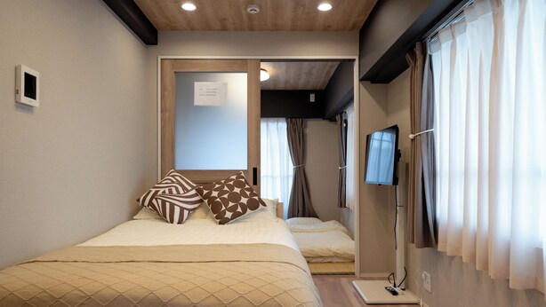 A bedroom with a bed, pillows, a TV, and a window with curtains. - Shinjuku commercial area-Shinjuku Area-East Shinjuku Shinjuku-2Room-Max5P-Japanese style-Ueno Shinjuku-Ikebukuro-Shibuya Direct access (新宿区新宿)