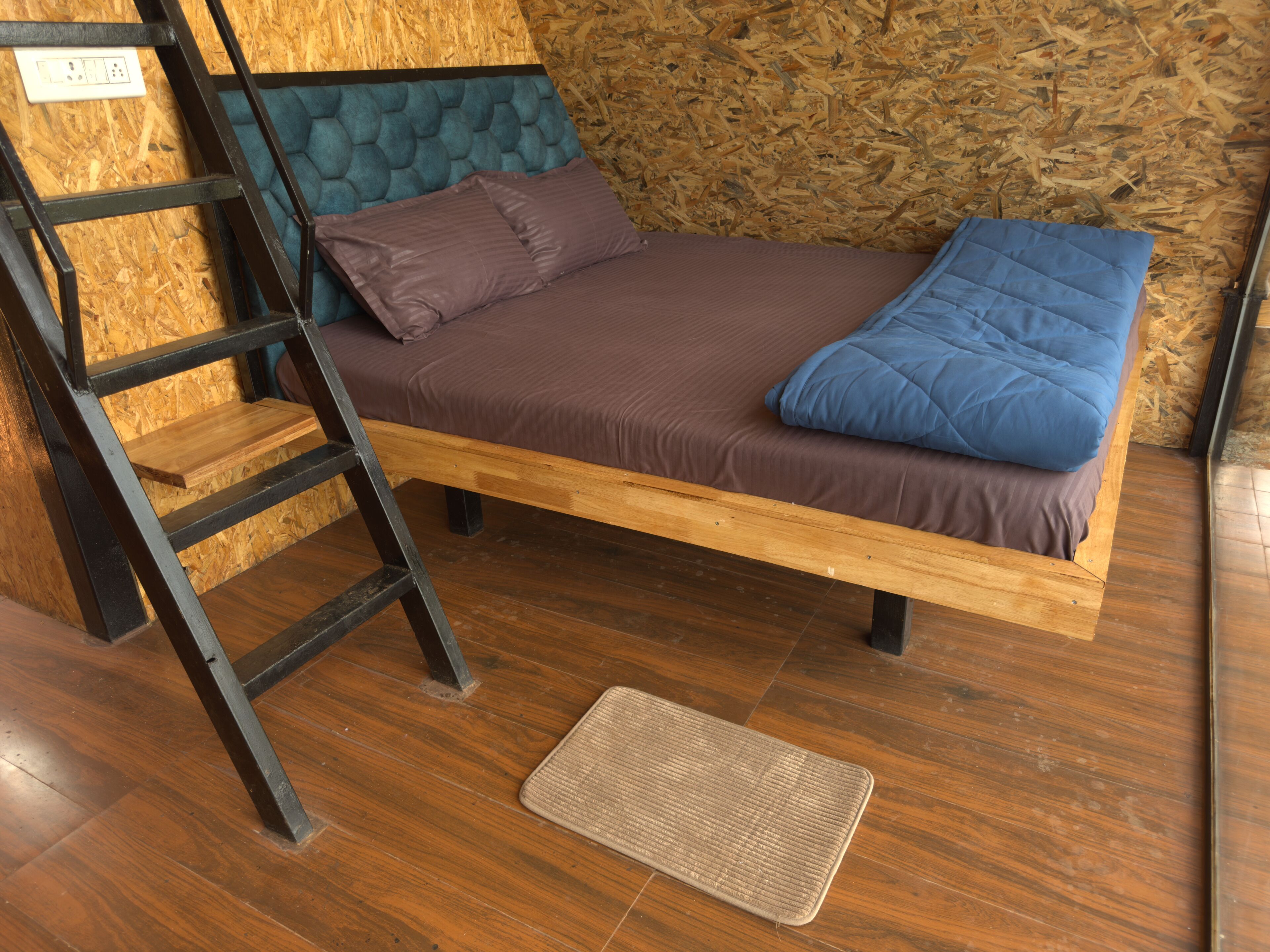 Uma cama de madeira com cabeceira, uma escada e um tapete de porta.