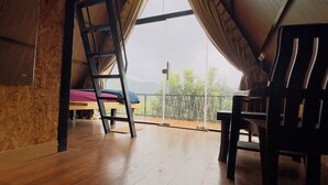 Habitación abuhardillada con techos altos, suelo de madera, una escalera y un gran ventanal con vistas a la vegetación.