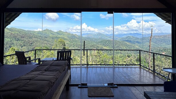 Una habitación con cama, una silla y una mesa, con vistas a un paisaje montañoso.
