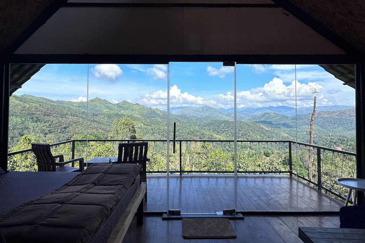 A room with a bed, a chair, and a table, overlooking a mountainous landscape.