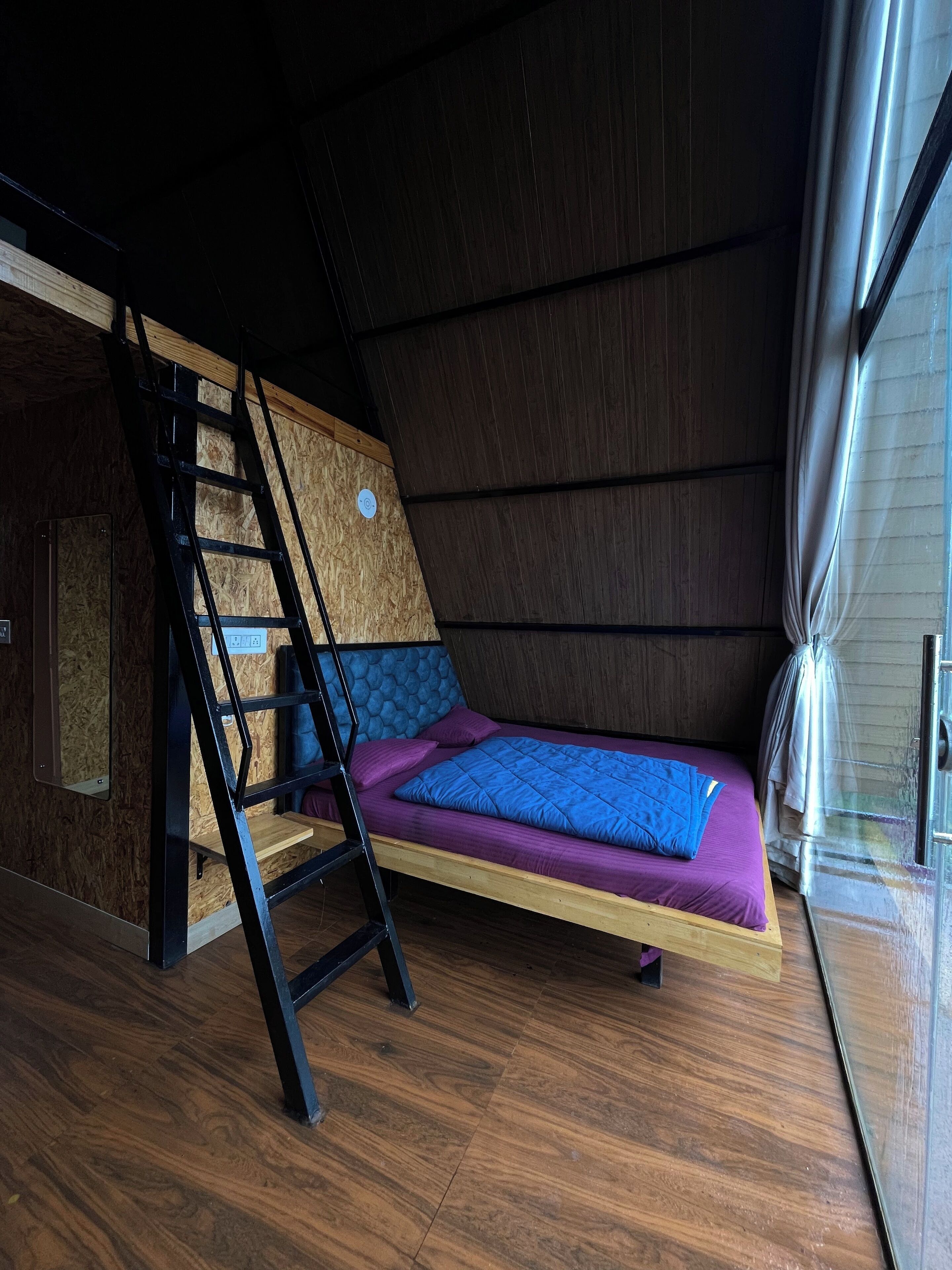 Dormitorio tipo loft con escalera de madera, literas y ventana con cortinas.