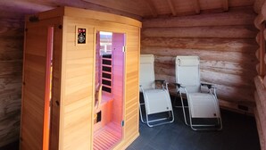 A sauna room with a wooden cabin, two reclining chairs, and a ceiling light.