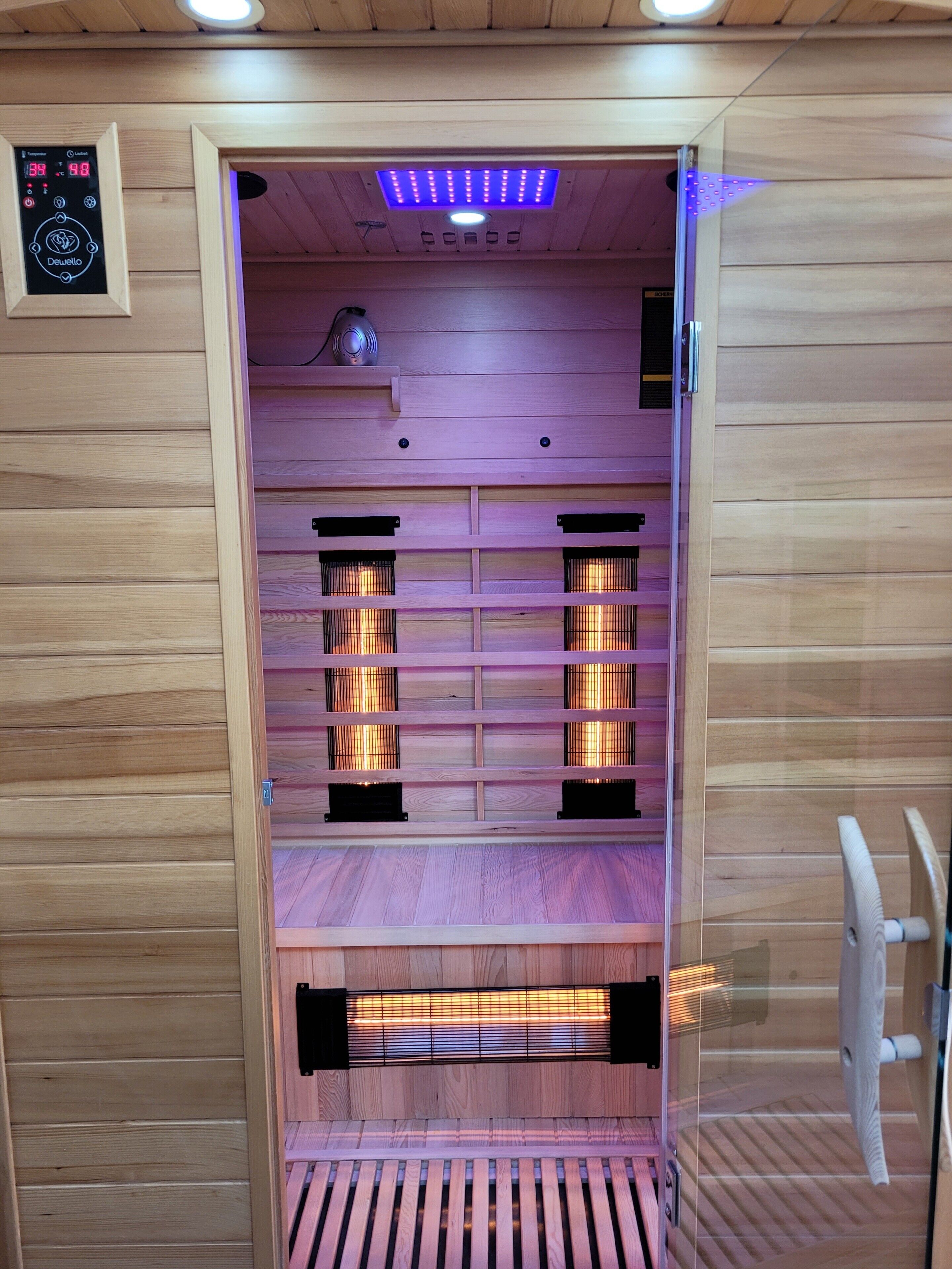 A sauna with wooden walls, a control panel, and multiple benches.