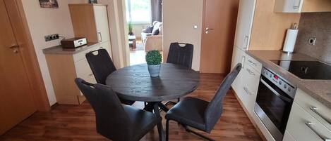 A compact kitchen with a dining table, chairs, a clock, and a stove.