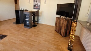 A room with a wooden floor, a desk with a chair, a TV on a wooden stand, and a poster of the Eiffel Tower.