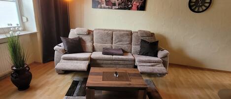 A living room with a sectional sofa, a coffee table, a clock, and a framed picture on the wall.