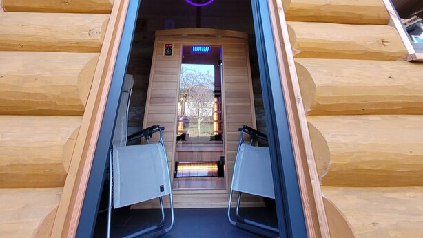 A wooden cabin with a sauna entrance, two chairs, and a visible control panel.
