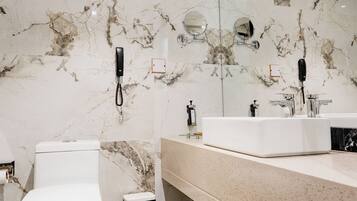A modern bathroom with a marble wall, a white toilet, a sink, and a trash bin.