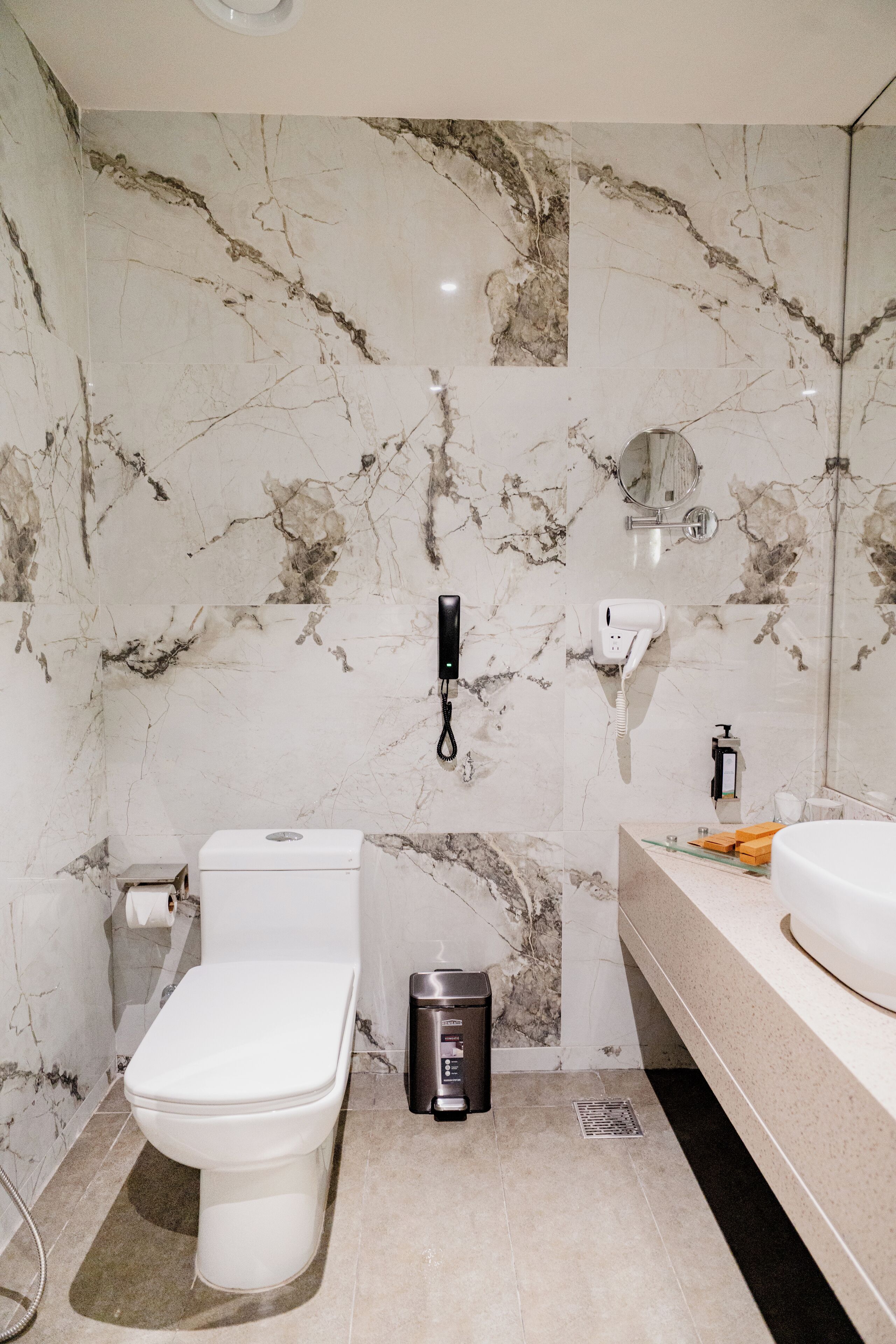 A bathroom with a toilet, a trash bin, a sink, and a mirror on the wall.