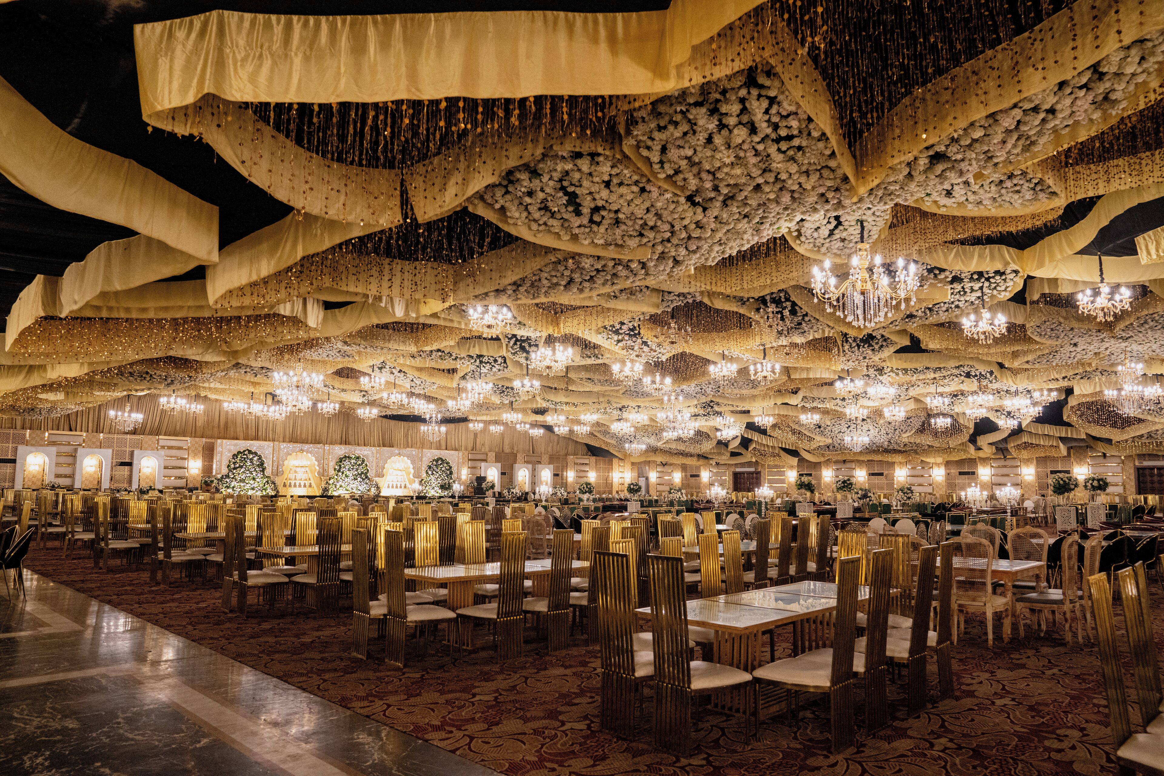 Un salón de banquetes con filas de mesas y sillas, candelabros y decoraciones colgantes.