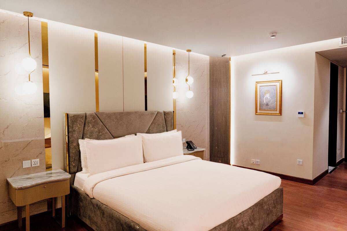 A modern hotel room with a large bed, bedside tables, a telephone, and a framed picture on the wall.