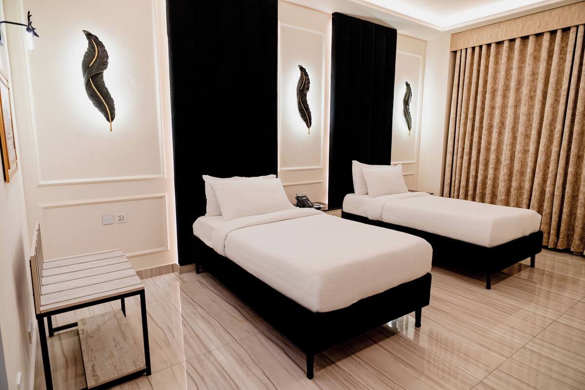 A hotel room with two single beds, a small table, and a large window with curtains.
