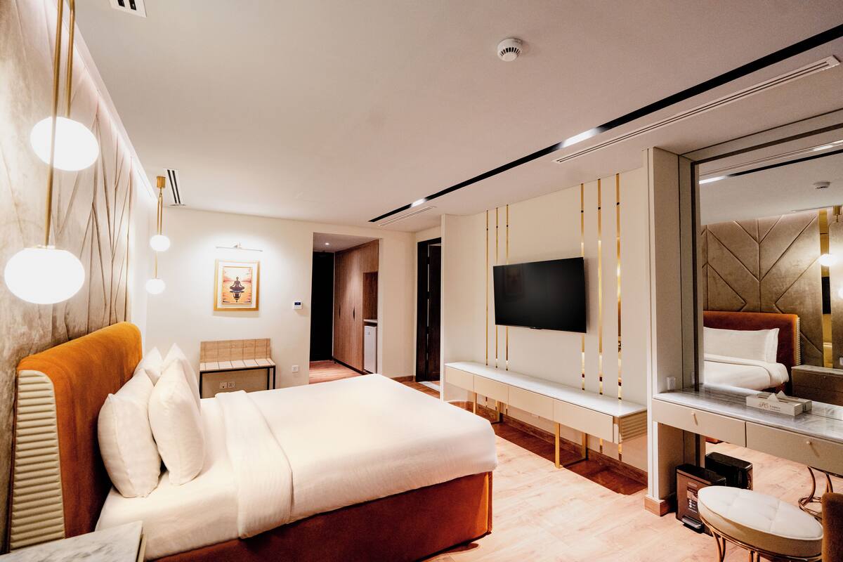 A modern hotel room with a large bed, a TV mounted on the wall, and a seating area with a small table and chair.