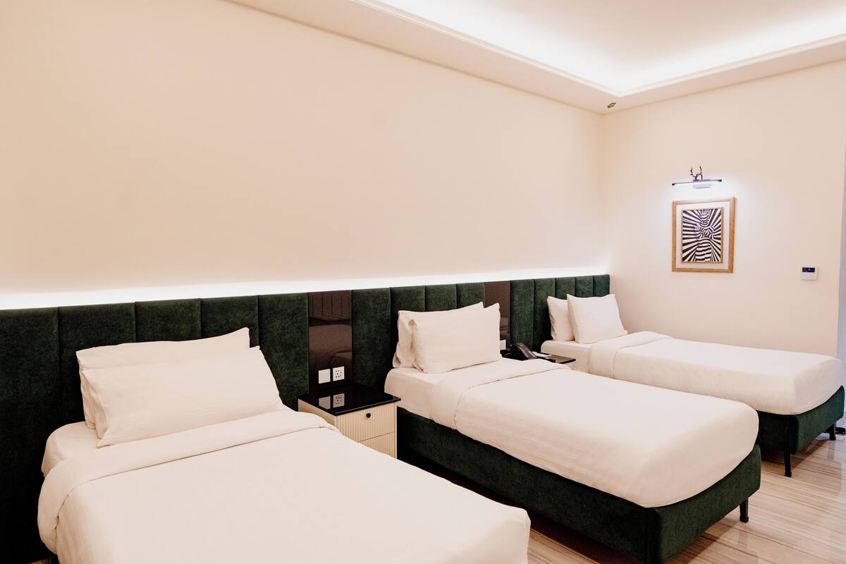 A hotel room with two single beds, a dark green headboard, a bedside table, and a wall-mounted light fixture.