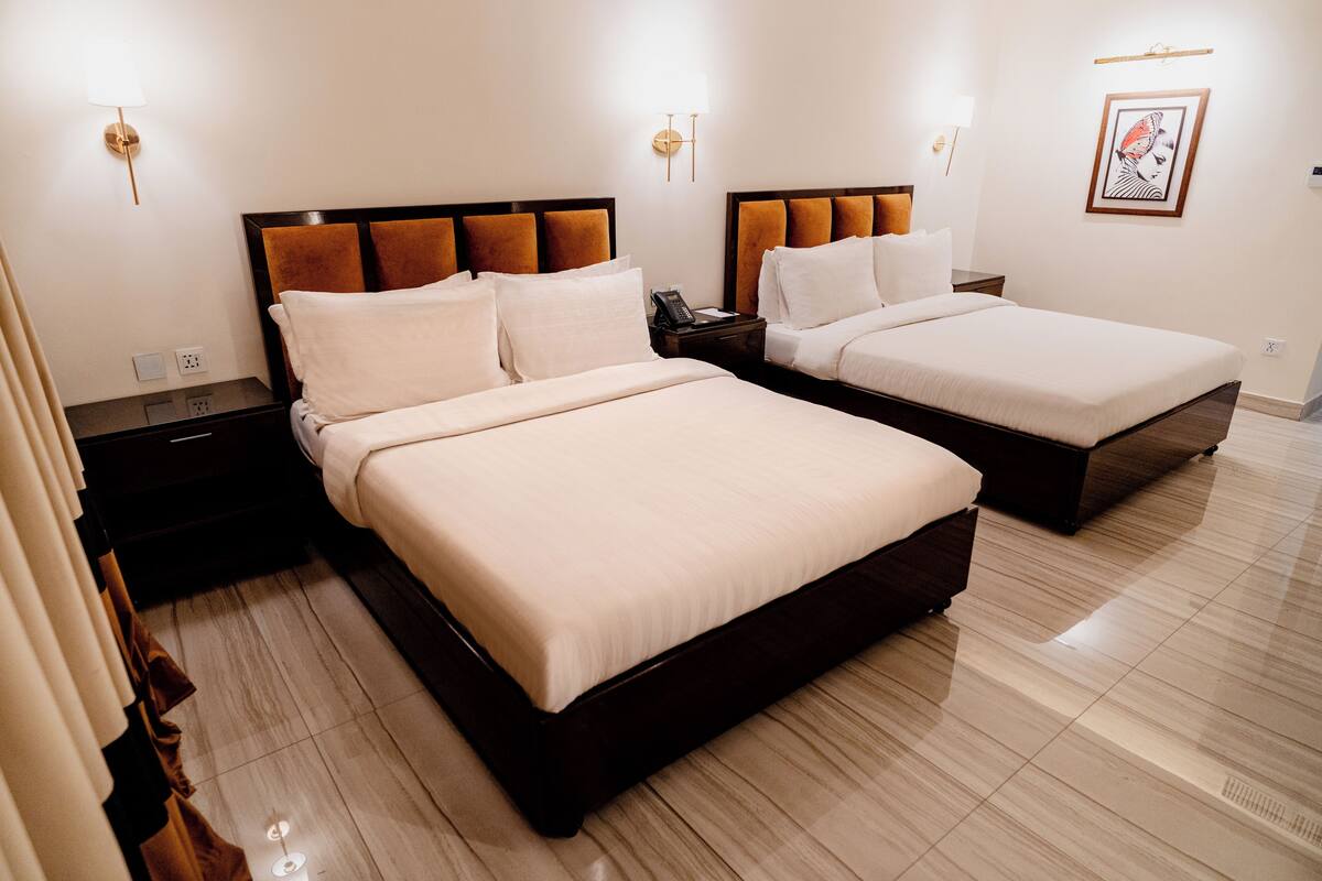 A hotel room with two beds, a nightstand, a lamp, and a framed picture on the wall.