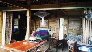 A rustic wooden cabin with a dining area, a bed with colorful bedding, and a hanging light fixture.