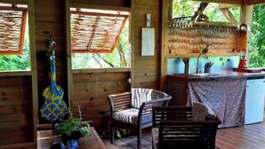 A wooden cabin with a dining area, a kitchen with a bar, and a large window overlooking greenery.