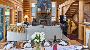 A log cabin interior with a fireplace, wooden beams, and a dining area set for a meal. - Black Bear Lodge (Snoqualmie Pass)