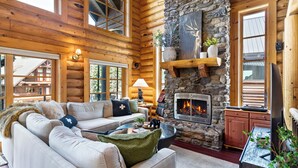 A log cabin interior with a stone fireplace, wooden walls, a sofa, and a television. - Black Bear Lodge (Snoqualmie Pass)