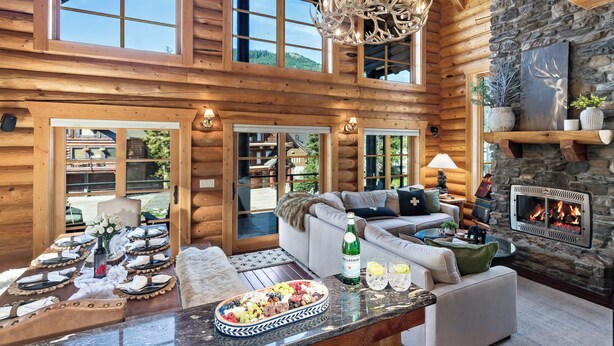 A log cabin interior with a stone fireplace, a dining area with a fruit platter, and a cozy seating area with a fireplace. - Black Bear Lodge (Snoqualmie Pass)
