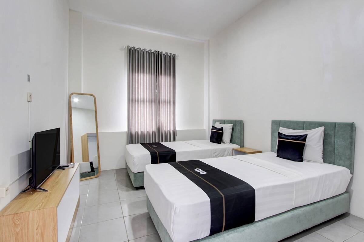 Habitación de hotel con dos camas, televisión, espejo y ventana con cortinas.