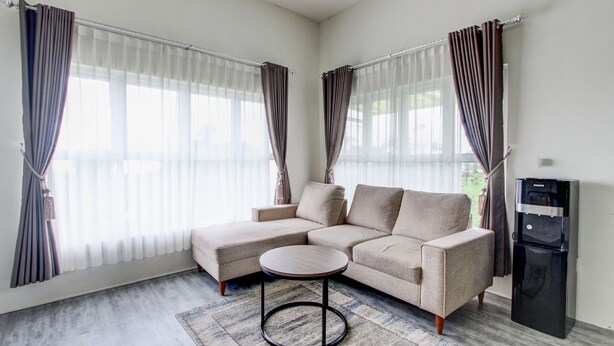 A modern living room with a sectional sofa, a round coffee table, and a refrigerator. - Capital O Sudirto Villa Dan Homestay Dieng (Wonosobo)