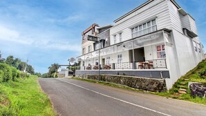 A two-story building with a balcony and outdoor seating area, located beside a road. - Capital O Sudirto Villa Dan Homestay Dieng (Wonosobo)