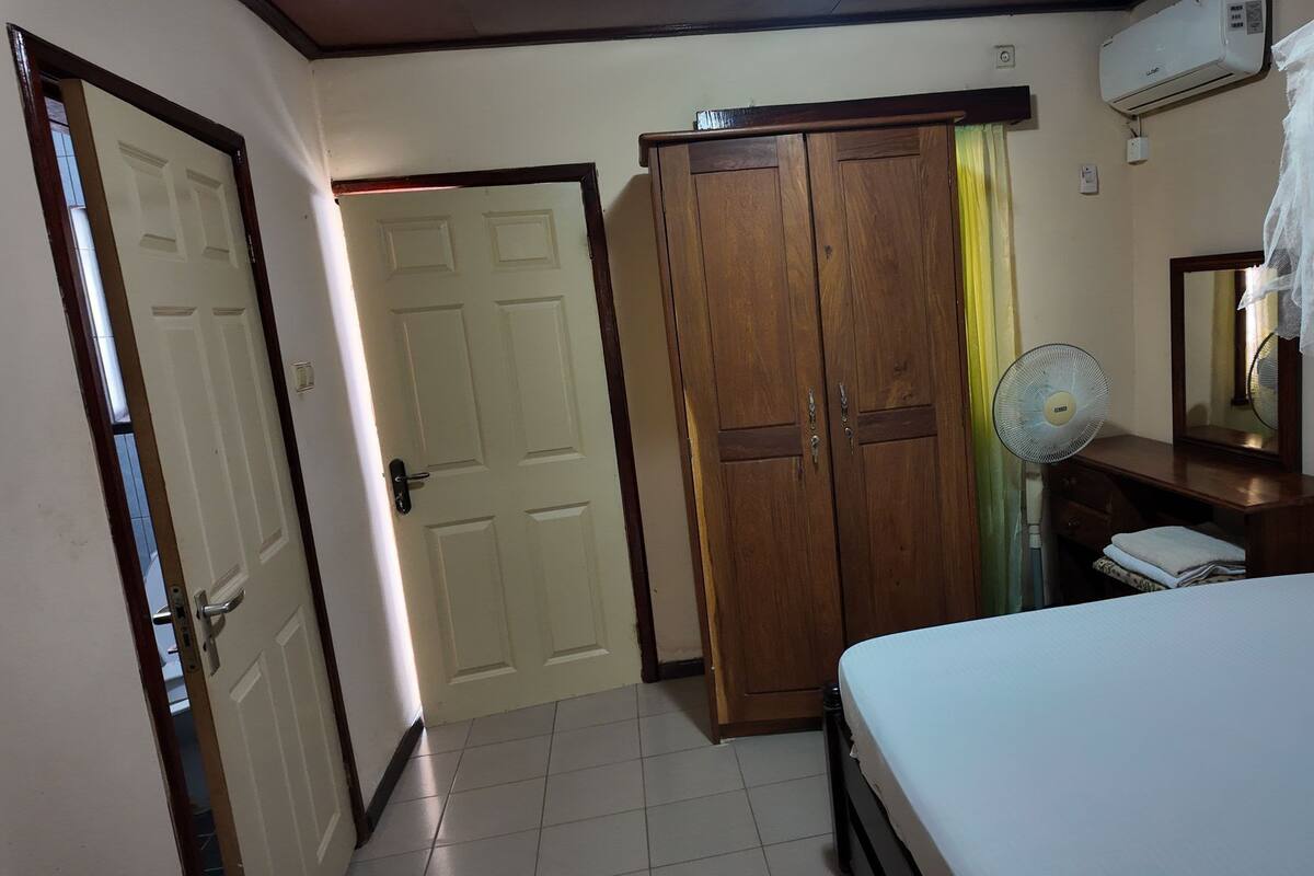 A bedroom with a bed, a wardrobe, a fan, and an air conditioning unit.