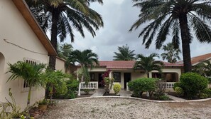 Una casa con tetto in tegole, circondata da palme e un vialetto sterrato.