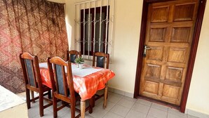 A dining area with a table set for four, a window with metal bars, and a wooden door. - Ocean Walk Guesthouse (Brufut)