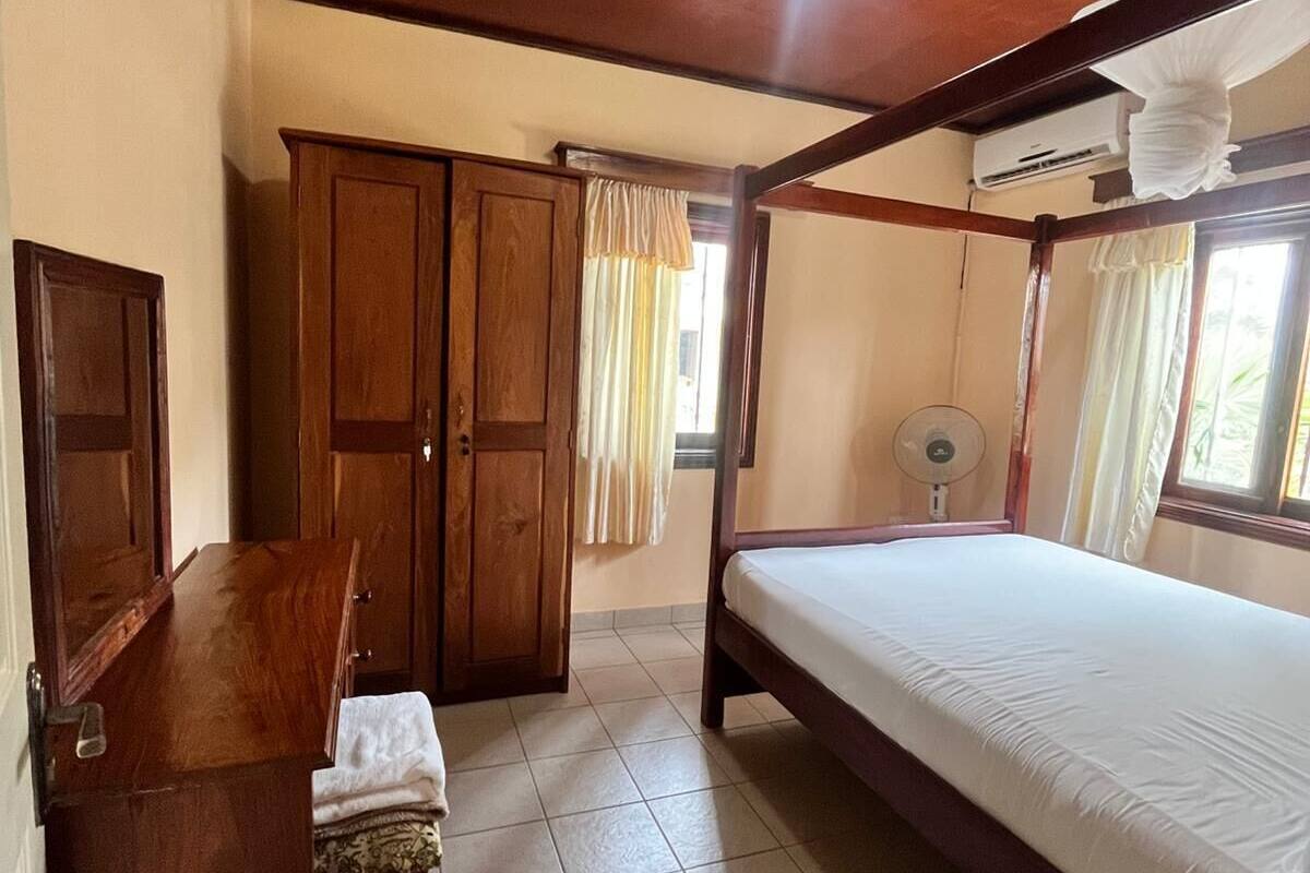 A room with a bed, a desk, a chair, a wardrobe, and a ceiling fan.