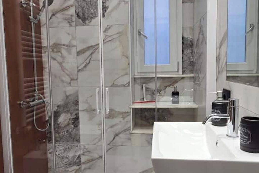 A modern bathroom with a glass-enclosed shower, marble tiles, a white sink, and a mirror.