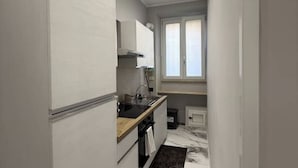 A compact kitchen with white cabinets, a black countertop, and a window providing natural light. - Feffo's home (Roma)