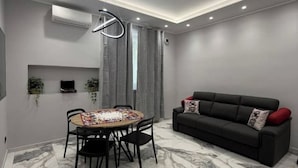 A modern living room with a black sofa, a dining table with chairs, and a ceiling light fixture. - Feffo's home (Roma)