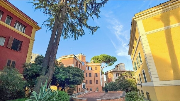 A courtyard with buildings, a tree, and a circular stone structure. - Feffo's home (Roma)