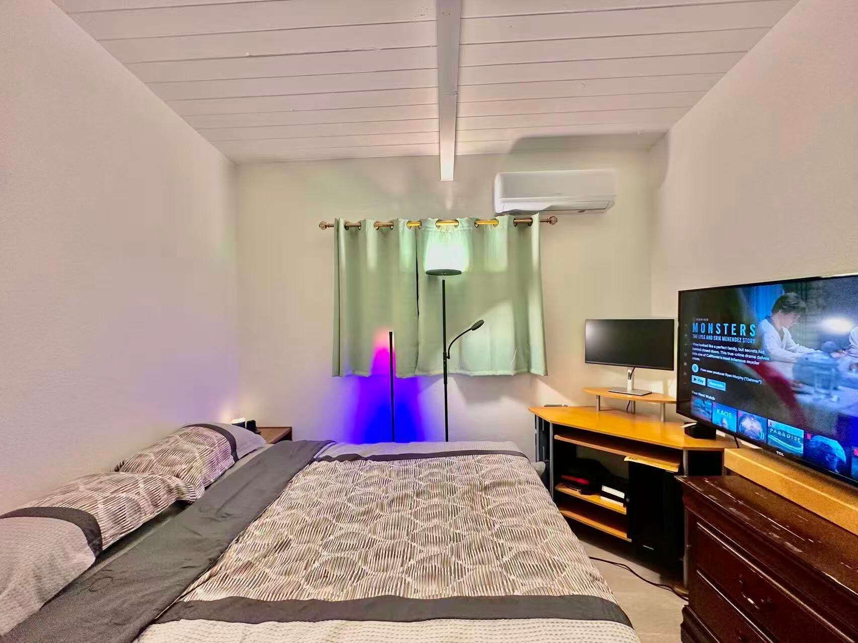 A bedroom with a bed, a TV, a desk, and a wardrobe.