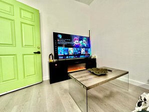 A modern living room with a flat-screen TV mounted on a black entertainment unit, a glass coffee table, and a green door. - Lime & Oak: Tech Ready 2BR Willow Glen
Oasis (San Jose)