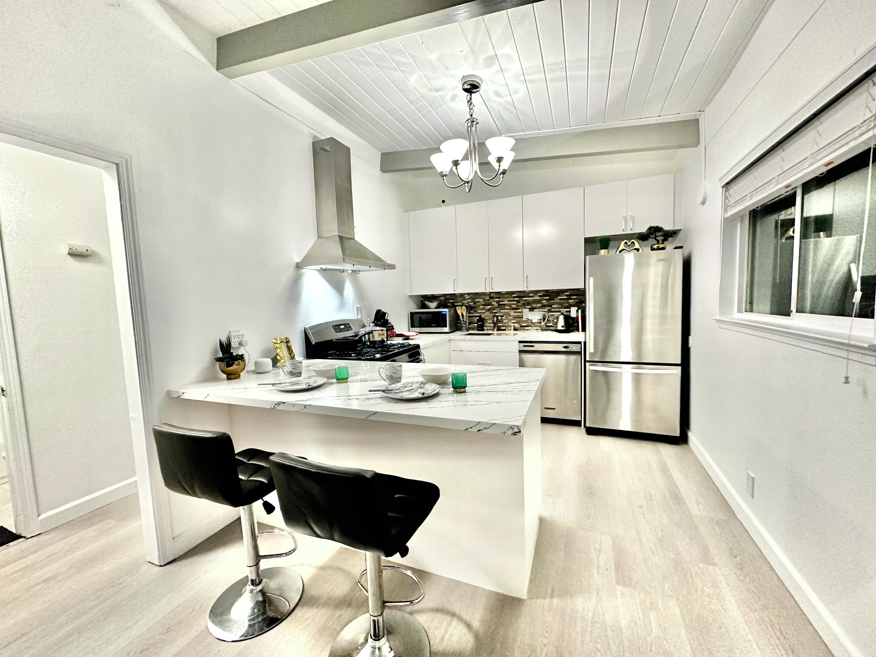 A modern kitchen with a central island, stainless steel appliances, and a chandelier.