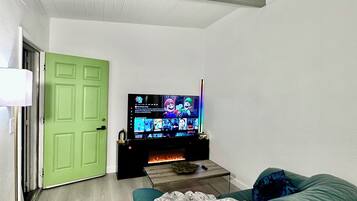 A living room with a green door, a flat-screen TV, a fireplace, and a green sofa.
