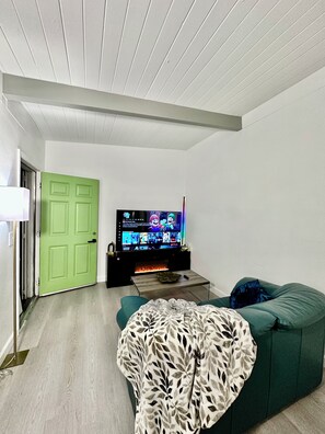 A living room with a green door, a flat-screen TV, a fireplace, and a green sofa. - Lime & Oak: Tech Ready 2BR Willow Glen
Oasis (San Jose)