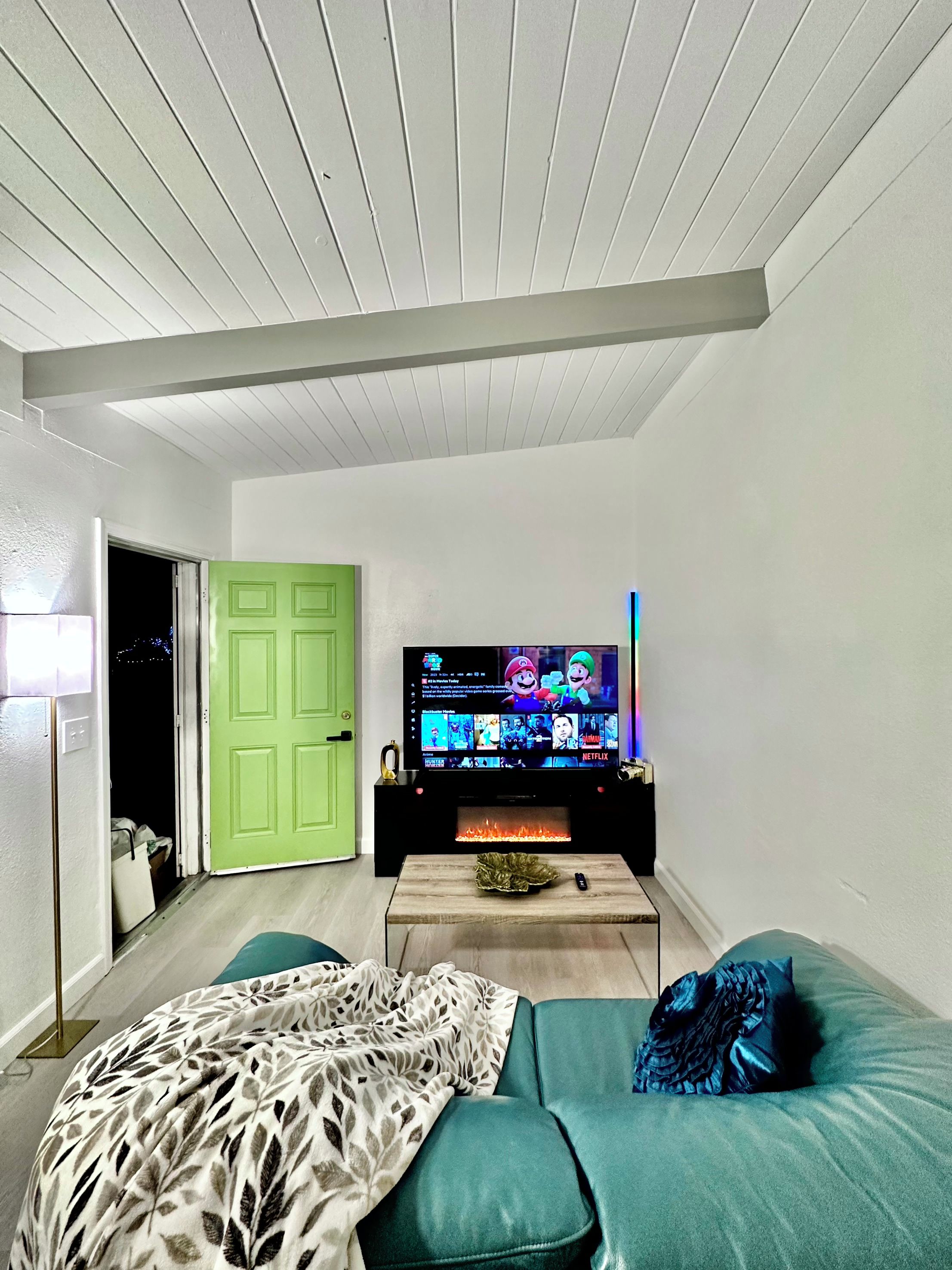 A living room with a flat-screen TV, a green door, and a sofa with a patterned throw.