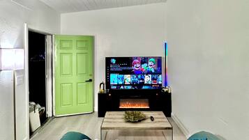 A living room with a flat-screen TV, a green door, and a sofa with a patterned throw.