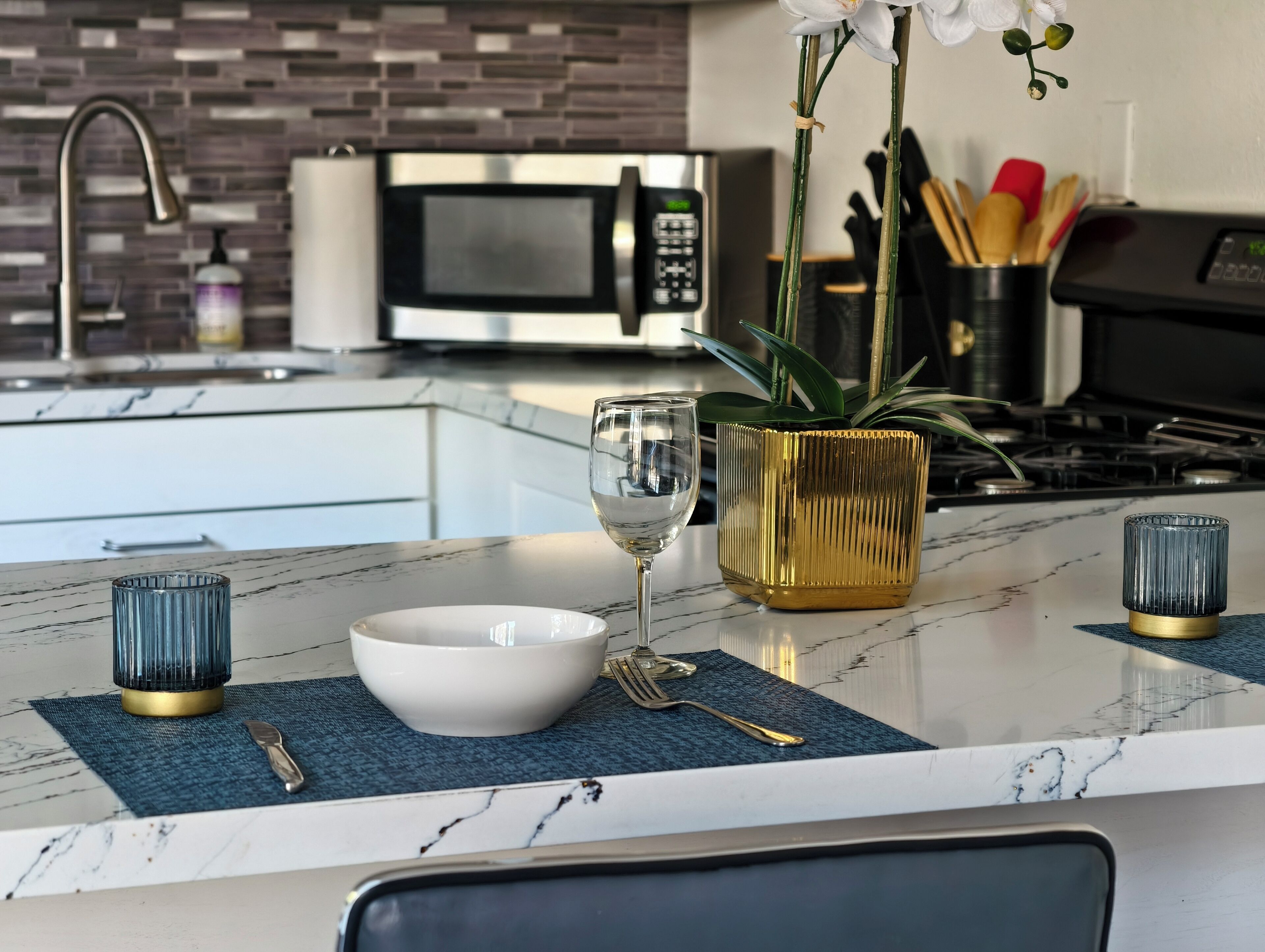 A modern kitchen with a marble countertop, a white bowl, a wine glass, and a gold vase with a plant.