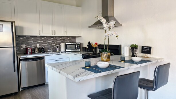 A modern kitchen with white cabinets, a stainless steel refrigerator, a microwave, and a central island with bar stools.