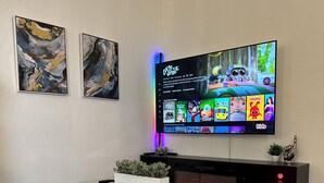 A modern living room with a flat-screen TV mounted on the wall, a glass coffee table, a sofa, and a fireplace.