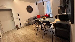Un espace de vie moderne comprenant un coin repas, un canapé avec des coussins rouges, une machine à café et une cuisine compacte.