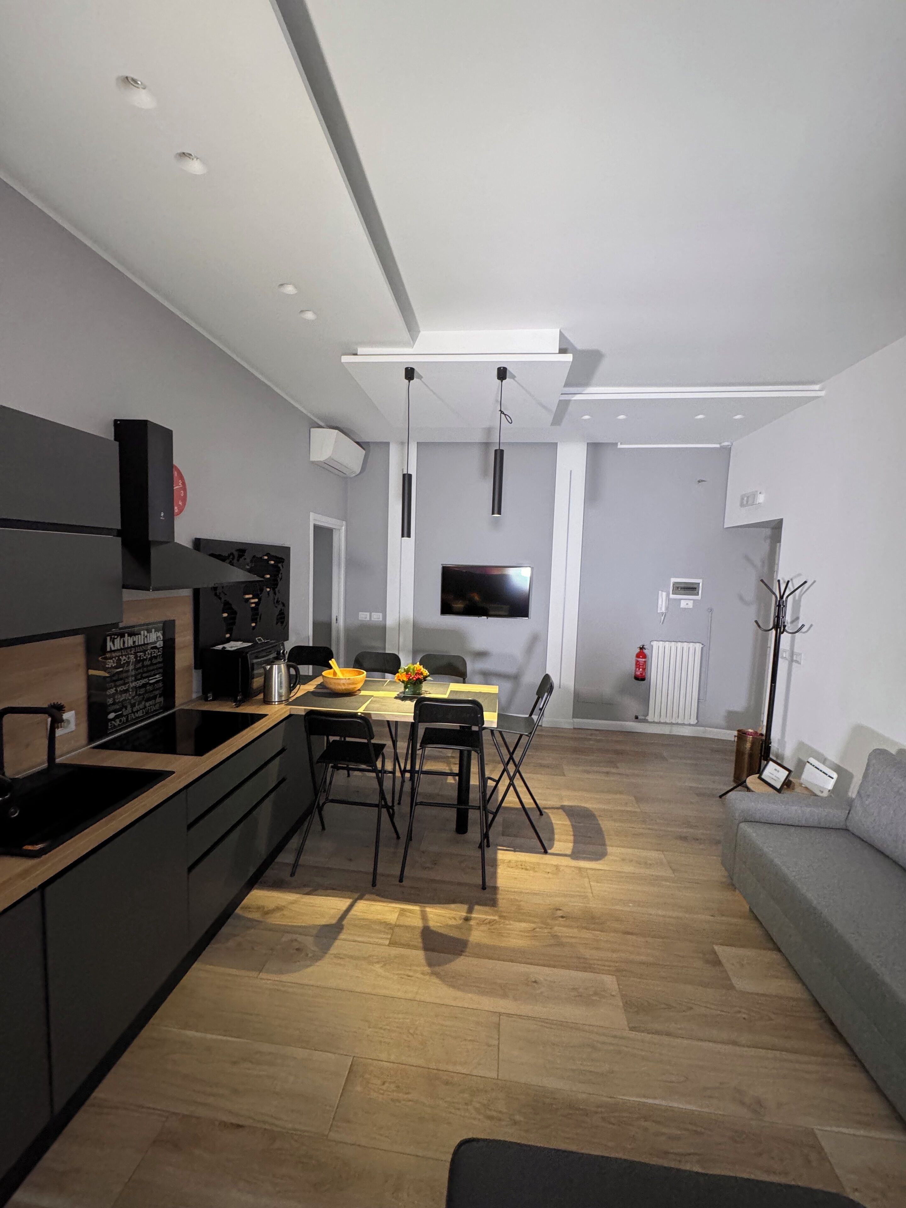 A modern kitchen with a dining area, wooden flooring, and a grey sofa.