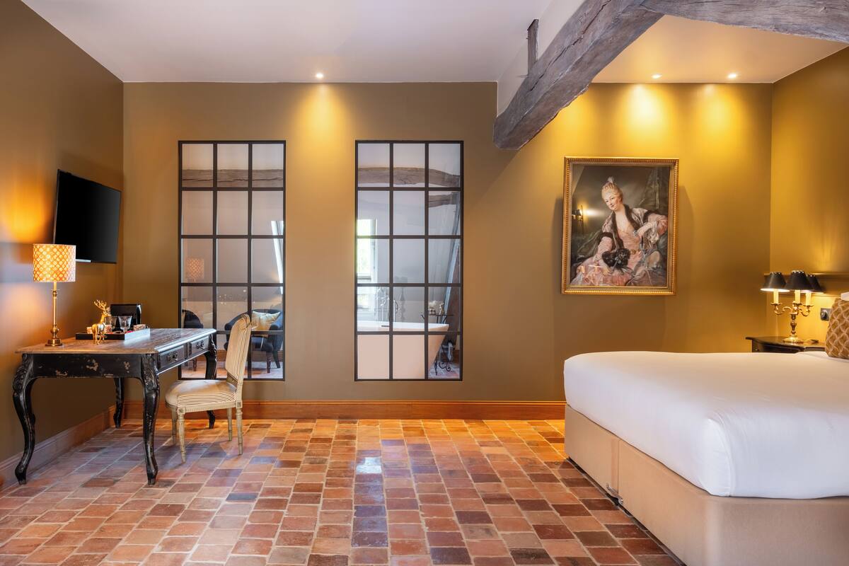 Een kamer met een bed, een bureau, een stoel, een schilderij en een groot raam.