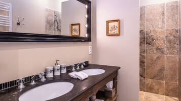 A bathroom with two sinks, a large mirror with lights, a towel rack, and a framed picture on the wall.